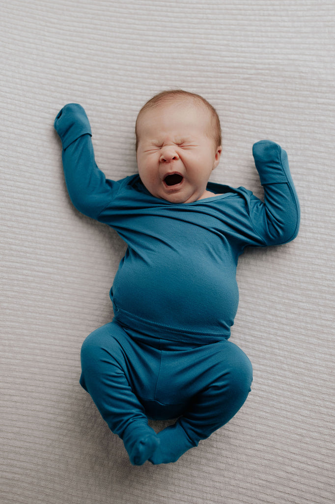 Cute newborn photoshoot with a yawning baby in Three Little Tots newborn pajamas with fold over mittens